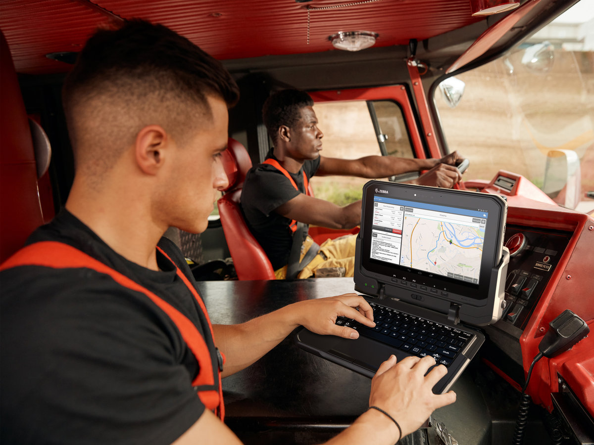 Two firefighters in the front cab of a firetruck in route to a scene, the passenger using an ET6 Series rugged tablet to check information. 